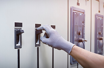 Worker wearing a safety glove switching an electrical control panel breaker